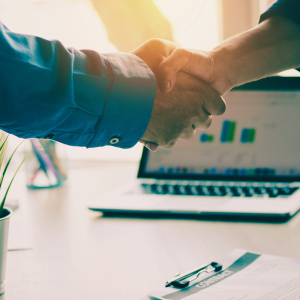 Two people shake hands across a desk.